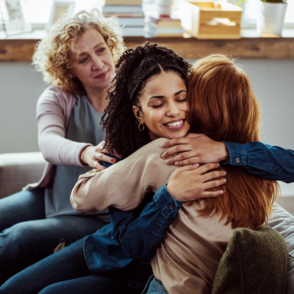 A smiling woman hugs another person warmly during an emotional group support session.