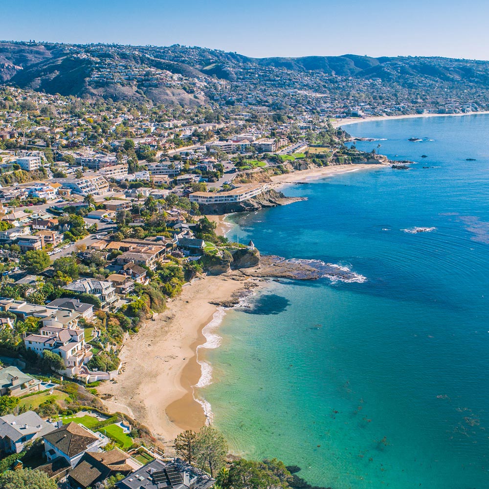 Aerial view of a coastal town with houses along the shoreline and clear blue ocean water.