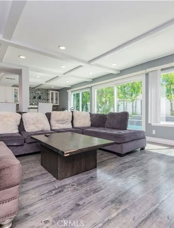 A bright living room with large windows, a gray sectional sofa, and a modern coffee table on wood flooring.