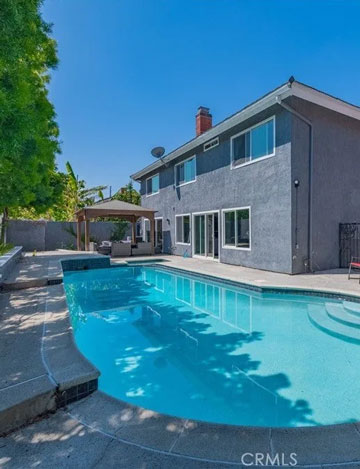 A modern gray two-story house with a backyard swimming pool and covered patio seating area under a clear blue sky.
